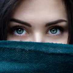 Ojos verdes penetrantes, enmarcados por cabello oscuro y un pañuelo. Un vistazo a la belleza que el microblading puede realzar.