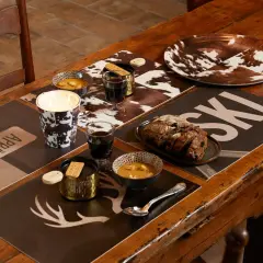 Ambiance chaleureuse pour une deco table raclette : bougie, bols de soupe, pain et verres de vin sur des sets "après ski" et motif vache.