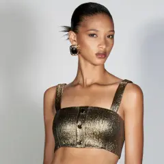 Modella con bronzer come si usa per un look radioso. Capelli raccolti, top dorato e orecchini neri.