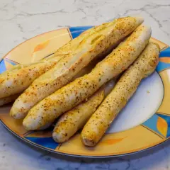 Leckere, knusprige brotstangen aus pizzateig, bestreut mit Gewürzen, liegen auf einem bunten Teller.