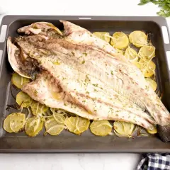 Corvina entera asada con patatas y limón en una bandeja. Una deliciosa opción para tus recetas de corvina.