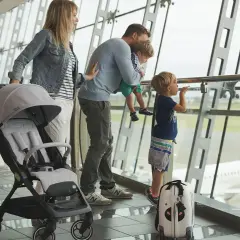 Famiglia in aeroporto, con passeggino e valigia, guarda un aereo. Speriamo che i bambini non soffrano di mal d'aereo!