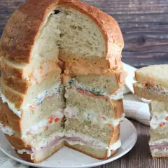 Un monumentale pane gastronomico a più strati, farcito con salmone, verdure e salse cremose, accanto a una versione più piccola.