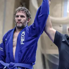 Tom Hardy i blå gi, med armen lyft som segrare i BJJ.
