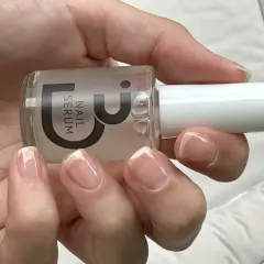 En hand håller en flaska nagelserum. Naglarna ser naturligt starkare och glansiga ut.