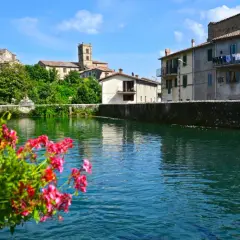 Fiori rossi in primo piano, con il borgo di Santa Fiora, Grosseto, che si specchia nell'acqua limpida.