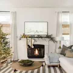Cozy living room with a lit Christmas tree and fireplace, showcasing elegant holiday mantel ideas with stockings and greenery.