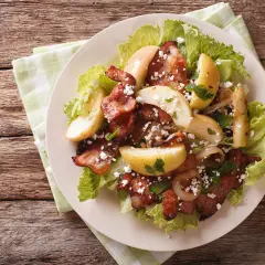 Une délicieuse idée de salade composée : lard croustillant, pommes de terre rôties, oignons caramélisés et fromage émietté sur un lit de laitue.