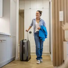 Uśmiechnięta kobieta z walizką w nowoczesnym mieszkaniu, gotowa na przeprowadzkę. To musi być najlepsza umowa najmu mieszkania!