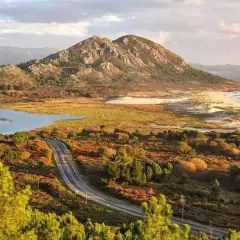Carretera serpenteante hacia el monte Louro, con un lago, dunas y el mar al fondo.