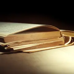 Stary, pożółkły tom leży otwarty. Strony lekko się unoszą, tworząc cień. Może to inspiracja, jak skleić książkę, by ocalić jej historię.