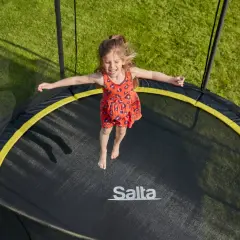 Ein fröhliches Mädchen springt auf einem Trampolin. Die Frage "Trampolin ab welchem Alter?" stellt sich hier nicht, denn Spaß kennt kein Alter!
