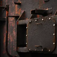 Dettaglio di una struttura metallica arrugginita, con tubi e una botola imbullonata. Un esempio di come trattare il ferro per non farlo arrugginire.