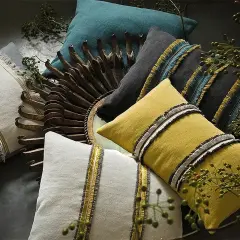 Stylowe poduszki w różnych kolorach, niektóre z frędzlami i złotymi akcentami, tworzą przytulną kompozycję. Miękki **aksamit** dodaje im elegancji.