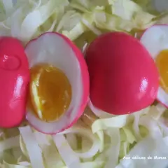 Trois œufs durs à la coquille rose vif, dont deux coupés révèlent un jaune d'œuf coulant, servis sur un lit de chou blanc émincé.
