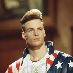 Homme blond avec une coiffure audacieuse, portant une veste aux couleurs du drapeau américain.