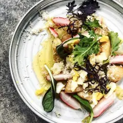 En vackert presenterad rätt med potatis, ägg, gröna blad och skivor av vit sparris, dränkt i en gyllene sås.
