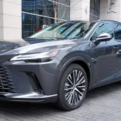 Elegancki, ciemnoszary Lexus RX 450h z nowoczesnym grillem i felgami stoi przed budynkiem biurowym.