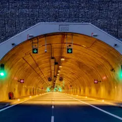 Wjazd do tunelu z kamienną górą w tle. Zielone światła sygnalizacyjne i znaki ograniczenia prędkości 80 km/h.