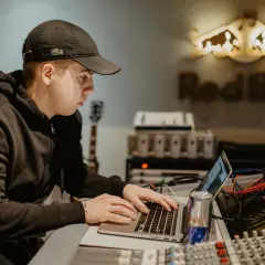 Un jeune beatmaker français concentré sur son ordinateur portable dans un studio d'enregistrement, une canette Red Bull à portée de main.