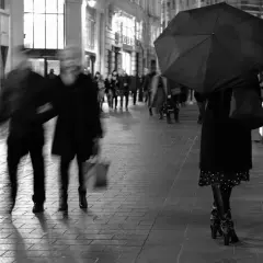 Nocne street photography. Rozmyte postacie spieszą się ulicą, jedna osoba z parasolką.