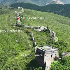 La muralla china se extiende por colinas verdes, con una torre de defensa y muros principales y subsidiarios.