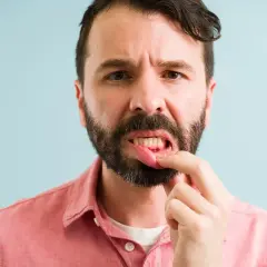 Hombre preocupado se toca la boca, mostrando encias sangrantes.