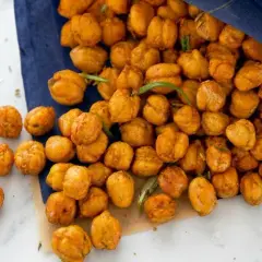 Knusprige Kichererbsen aus dem Ofen, goldbraun und mit Kräutern verfeinert, liegen auf einem blauen Tuch.