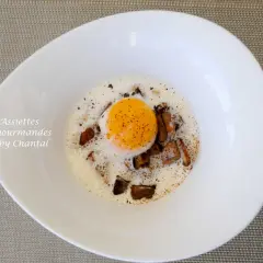 Un œuf poché, entouré de morceaux de champignons et d'une mousse légère, dans une assiette blanche. Des oeufs parfaits pour un repas gourmand.
