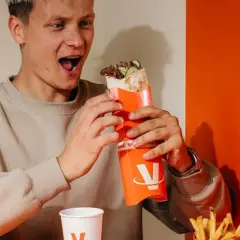 Młody mężczyzna z zachwytem trzyma w rękach viral kebab. Jego mina sugeruje, że opinie o tym daniu są w pełni uzasadnione.