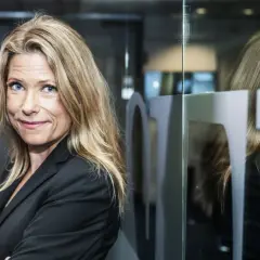 Petra Nordlund, med sitt blonda hår och blå ögon, ler mot kameran. Hon bär en svart kavaj och står framför en glasvägg med en spegelbild.