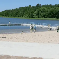 Słoneczne plaże na Mazurach przyciągają ludzi. Dzieci bawią się na piasku, a dorośli spacerują po pomoście.