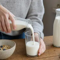 Versando latte fresco, ricco di grassi del latte, in un bicchiere per accompagnare i cereali con mirtilli.