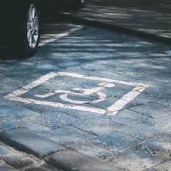 Wyznaczone miejsce parkingowe dla niepełnosprawnych pod blokiem. Symbol wózka inwalidzkiego na niebieskim tle.