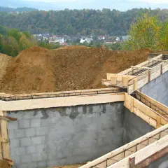 Fundament budowy z zbrojeniem i szalunkiem, w tle domy i las.