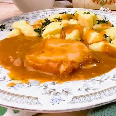Pyszny schab w sosie, podany z kluskami śląskimi i posypany koperkiem. Danie prezentuje się apetycznie na ozdobnym talerzu.
