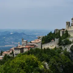 San Marino na terytorium Włoch, z górującymi wieżami i kamiennymi murami, wznosi się dumnie na skalistym szczycie, otoczone zielonymi wzgórzami.