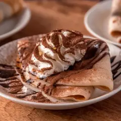 Deliziose crepes senza uova, guarnite con panna montata, cacao e sciroppo al cioccolato, un piacere per gli occhi e il palato.