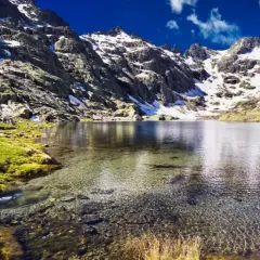 Espectacular vista de la ruta laguna grande de Gredos, con montañas nevadas, césped verde y aguas cristalinas.