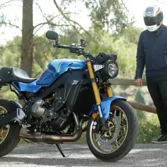 Motocicleta azul de estilo neo retro con detalles dorados, aparcada junto a un hombre con casco.