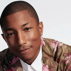 Pharrell Williams w kwiecistej marynarce, uśmiecha się, emanując pozytywną energią, jak w tekście "Happy".