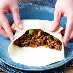 Hände falten wraps mit Hackfleisch, Bohnen und Mais. Ein leckerer Snack wird zubereitet.