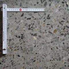 Superficie di calcestruzzo a vista con aggregati di varie dimensioni. Un righello pieghevole misura la **classe di esposizione calcestruzzo**.