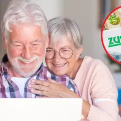 Uśmiechnięta para seniorów przegląda dokumenty ZUS na laptopie, planując wcześniejszą emeryturę.