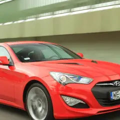 Czerwony Hyundai Genesis Coupe pędzi pod zielonym wiaduktem.