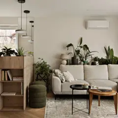 Jasny beżowy salon z dużą ilością roślin. Wygodna kanapa, drewniane meble i stylowe dodatki tworzą przytulną atmosferę.