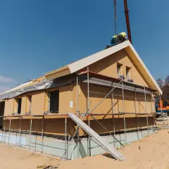 Budowa domu z prefabrykowanych elementów. Widoczna ściana drewniana szkieletowa, rusztowania i pracownicy na dachu.