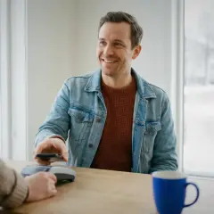 Uśmiechnięty mężczyzna płaci telefonem w Szwecji. Choć gotówka jest rzadkością, nadal można nią płacić.