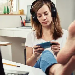 Kobieta w słuchawkach gra na telefonie, nogi na biurku. Czy to prokrastynacja co to?
