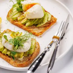 Zwei Scheiben Toast mit Avocado und pochiertem Ei, garniert mit Sprossen. Ein köstliches Egg Benedict Avocado Gericht.